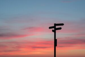 A directional sign pointing in 3 different directions in the shadow of a sunset